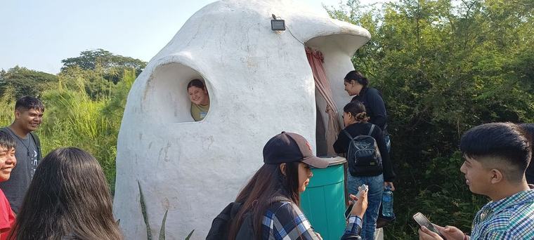 Grupo sonriente junto a una construcción circular de bahareque en un evento anterior de Pakkitlán
