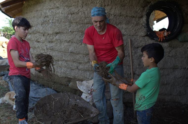 Adulto y dos jóvenes trabajando juntos con bahareque en un muro